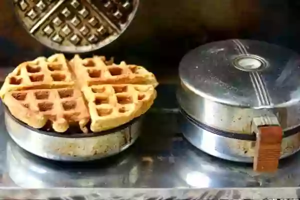 2 old school waffle makers with one open showing a fully cooked belgian waffle. 