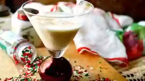feature image of the low carb christmas cookie martini sitting on a wooden cutting board surrounded by red and green sprinkles. A scarf is in the background.
