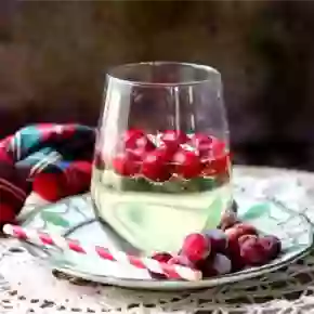 square image of a glass of low carb white wine spritzer with frozen cranberries floating in it. A green and red plaid napkin is in the background