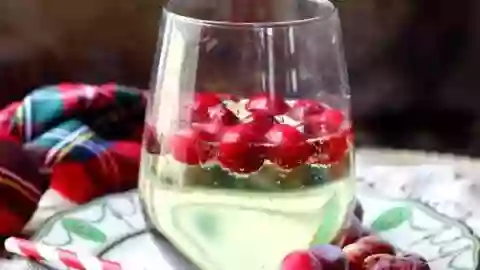 square image of a glass of low carb white wine spritzer with frozen cranberries floating in it. A green and red plaid napkin is in the background