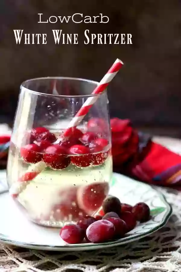 Low carb white wine spritzer title image - cocktail is in a clear balloon glass with frozen cranberries and a red and white straw.