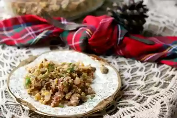 Feature image - a plate of low carb stuffing sits on a lace covered table with a red plaid napkin in the background. The plate has gold trim