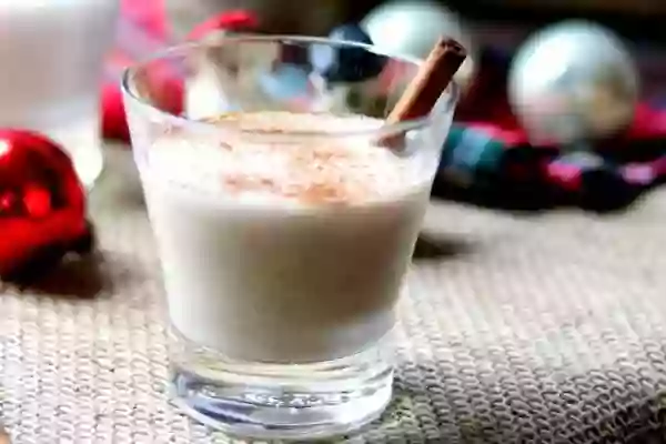 Low carb coquito without eggs in an on the rocks glass with cinnamon sticks. Ornaments int he background