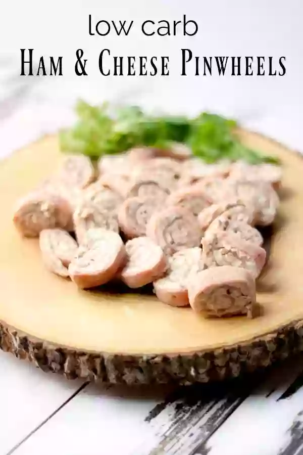 A rough wood platter full of low carb ham pinwheels placed on a chippy white wood surface