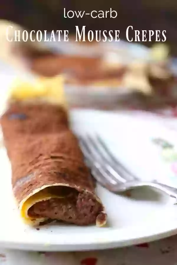 close up of low carb chocolate mousse crepes, dusted with cocoa and placed on a white plate with a silver fork. TItle image