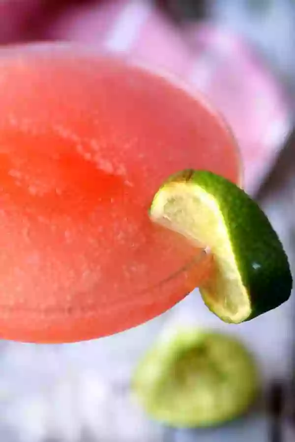 Close up of the slushy top of a skinny watermelon margarita with a lime wedge on the side of the glass.