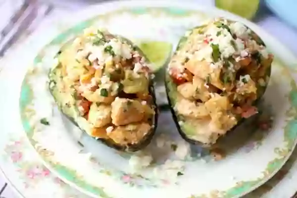 Two halves of southwestern chicken salad in avocado shells on a vintage pink and green plate - feature image