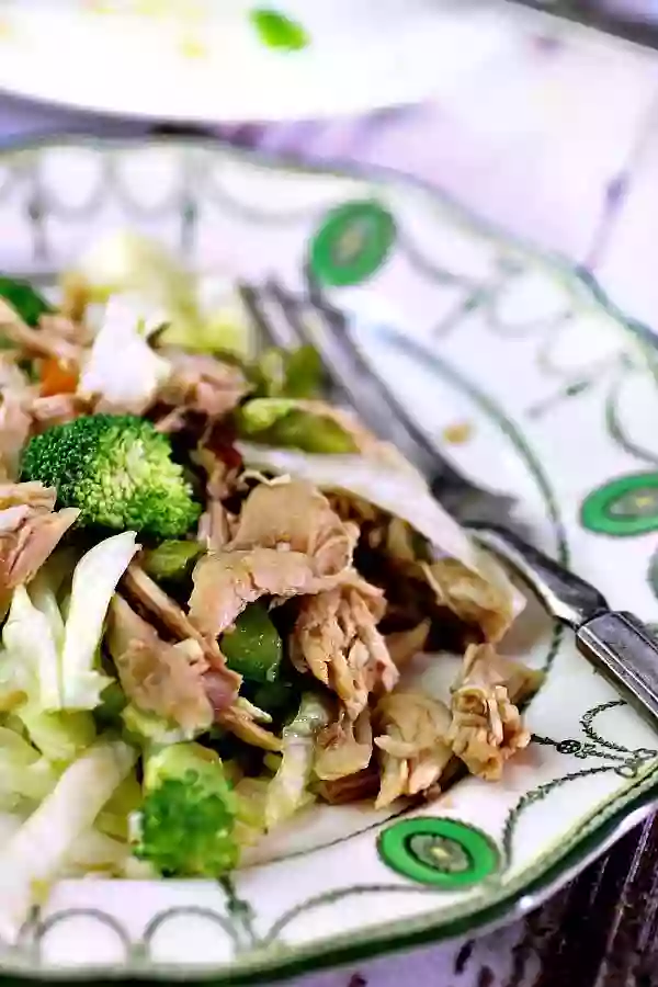 Hunan Chicken salad is served on a white and green plate with a silver fork.