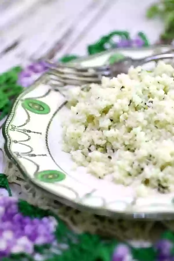 A closeup of a serving of low carb cilantro lime cauliflower rice on a vintage plate with a fork in the background.