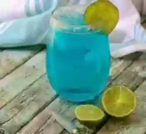 A horizontal image of a low carb cocktail, Ocean Breeze, garnished with lime. A cut lime is on the table.