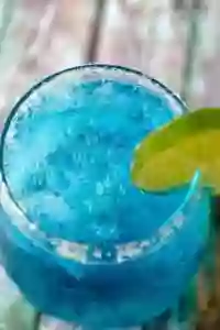 Closeup of the Bright Blue Low Carb Cocktail Ocean Breeze. a Lime Wheel Garnishes the Glass.