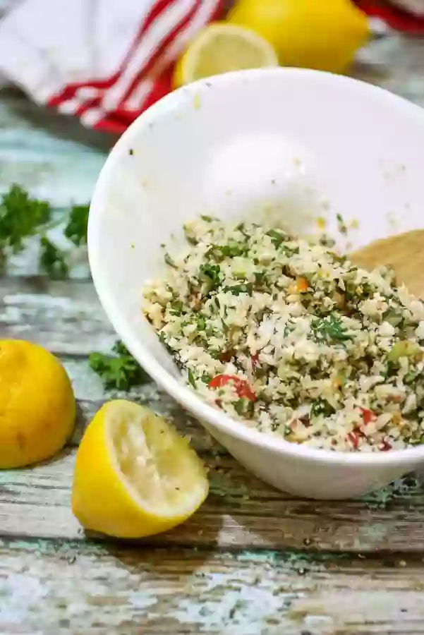 A white bowl with the finished tabbouleh recipe in it. Cut lemons are to the side.