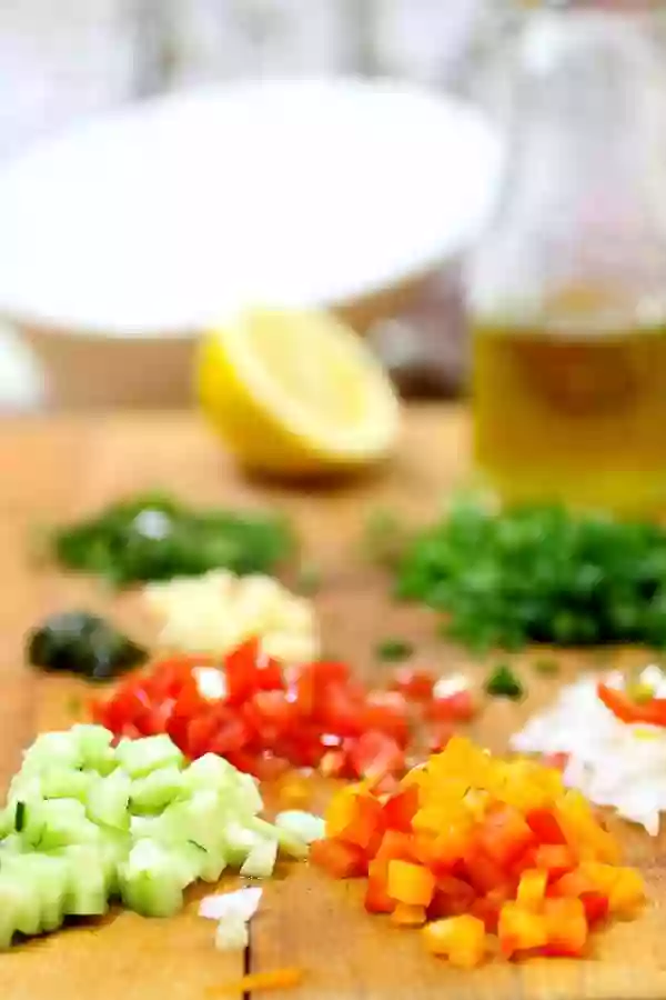 Small piles of diced cucumber, pepper, tomato, onion, and other ingredients on a cutting board.