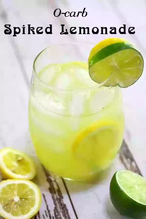 Glass of spiked lemonade on a white table with lemon and lime halves at the foot of the glass.
