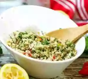 Cauliflower tabbouleh salad in a white bowl with a wooden spoon.