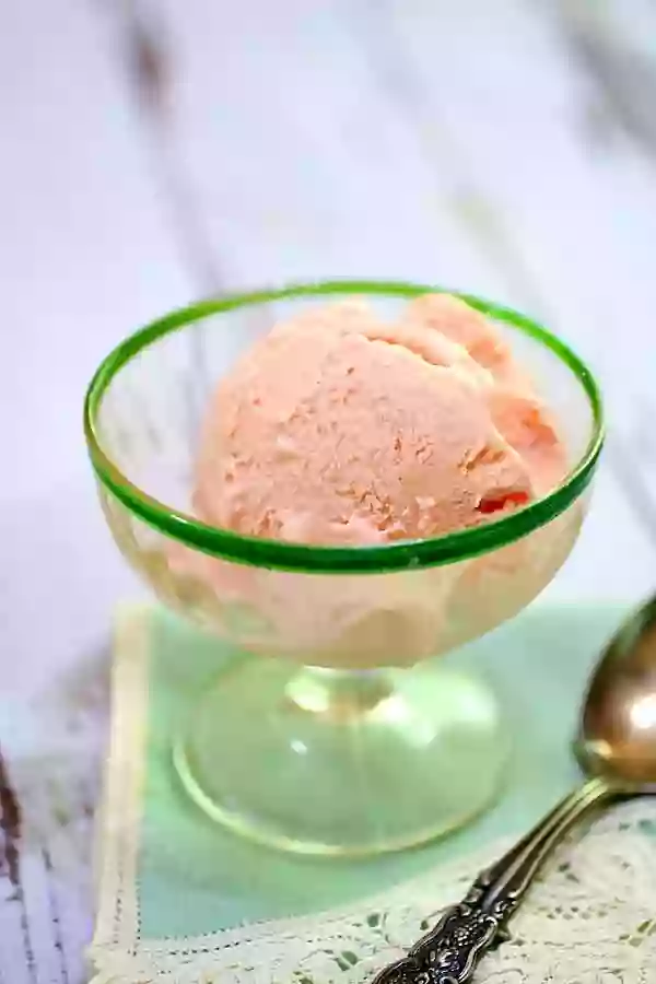 A scoop of pin strawberry ice cream in a vintage vaseline glass footed sherbet dish.