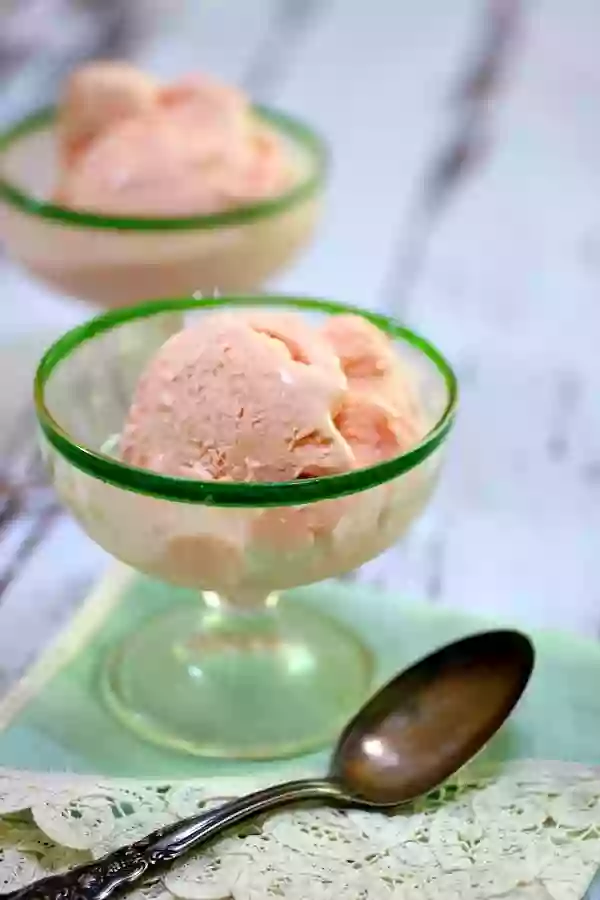 Two ice cream dishes with a scoop of strawberry ice cream in each.
