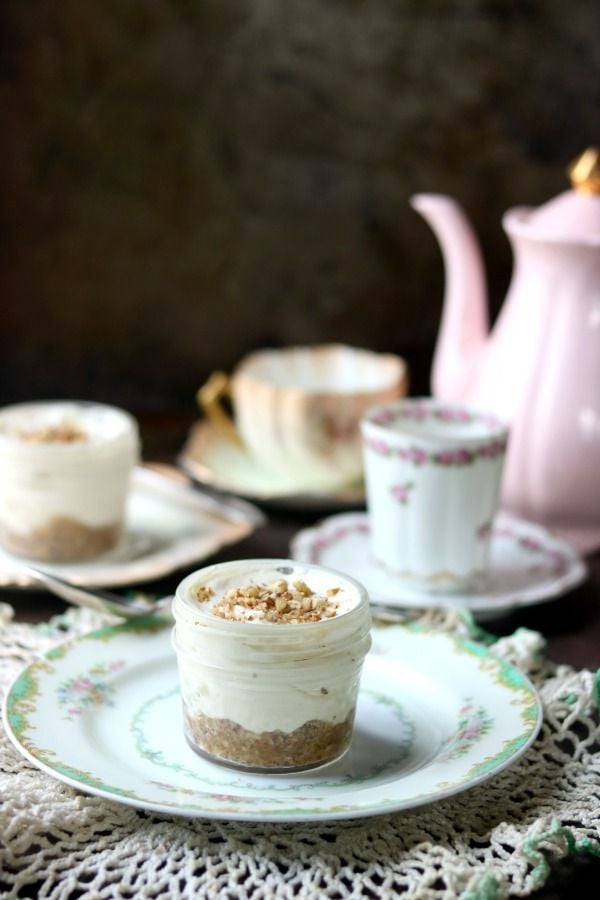Pink teapot and vintage dishes with two small servings of low carb caramel pecan cheesecake on a lace cloth.