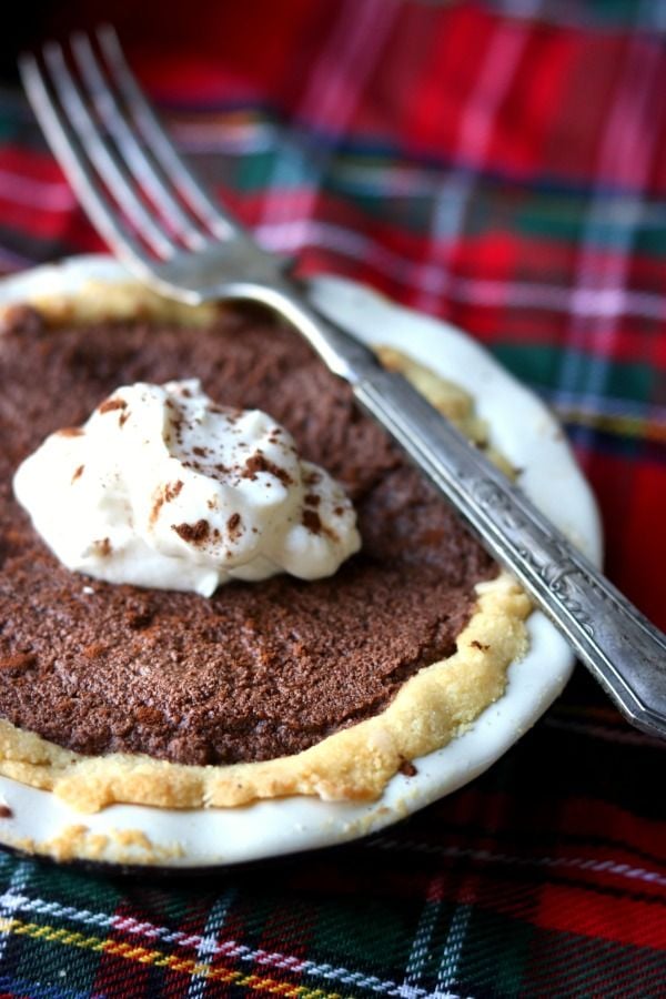 a low carb french silk pie sits on a red and green plaid table cloth. A sliver fork rests on the pie dish.
